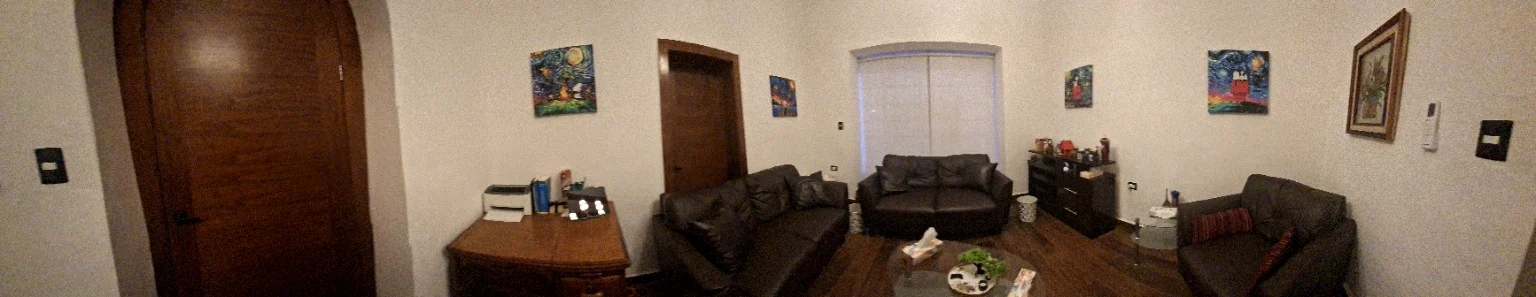 Fotografía panorámica auténtica del consultorio de psicología con dos puertas, escritorio y área de atención